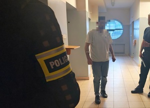 Pomieszczenie dla osób zatrzymanych, policjant z opaską Policja czeka na zatrzymanego, który wychodzi z celi.
