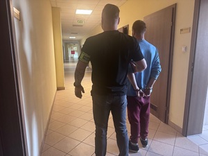 Nieumundurowany policjant, prowadzący zatrzymanego w kajdankach.