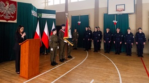 Dyrektor szkoły stoi przy mównicy, przemawia do zebranych. W tle stoją kadeci i poczet sztandarowy.