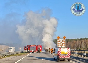 Droga, dym, w poprzek drogi stoi samochód strażacki, a obok służby drogowe.