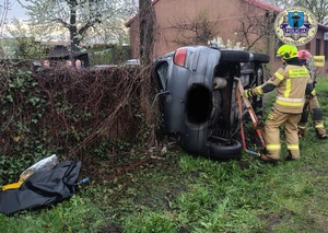 Auto lezy na boku, obok stoi dwóch strażaków.