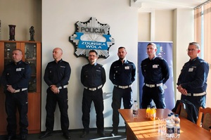 Pod ścianą, w rzędzie stoją policjanci.