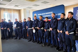 Pod ścianą, w rzędzie stoją policjanci.