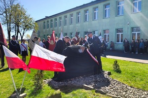 Tablica pamiątkowa z nazwiskami pomordowanych odsłaniana przez komendanta i wójta. W tle budynek szkoły.