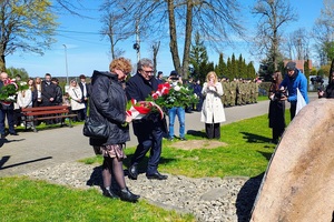 Dwie osoby składają kwiaty pod tablicą.