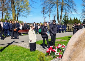 Troje dzieci stawia znicz pod tablicą.