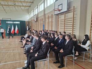 Uczniowie siedzą na krzesełkach w sali gimnastycznej.