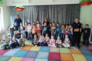 Grupowe zdjęcie dzieci i policjantów. Wszyscy stoją pod ścianą i pozują do zdjęcia.
