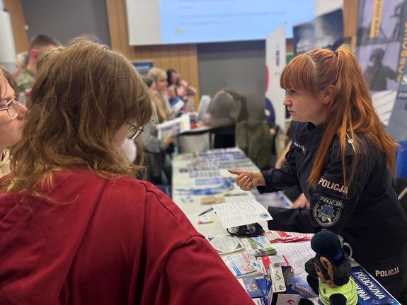 Policjantka rozmawia z młodzieżą, pokazuje ulotkę.