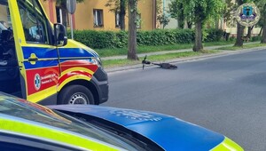 Na jezdni leży przewrócona hulajnoga, obok karetka pogotowia i radiowóz.