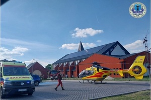 Plac, na jego środku stoi helikopter, w tle kościół, obok karetka pogotowia.