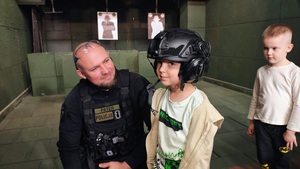 Policjant pozuje do zdjęcia z chłopcem, który ma na głowie założony hełm strzelecki.