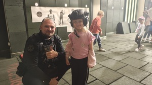 Policjant pozuje do zdjęcia z dziewczynką, która ma na głowie założony hełm strzelecki.