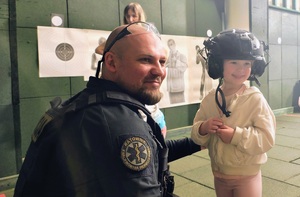 Policjant pozuje do zdjęcia z dziewczynką, która ma na głowie założony hełm strzelecki.