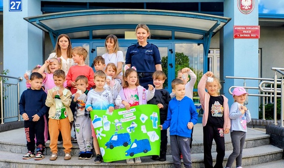 Grupowe zdjęcie przedszkolaków i policjantki na schodach przed komendą.