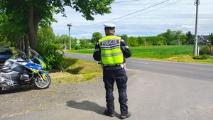 Policjant stoi przy drodze, obserwuje jak jeżdżą samochody.