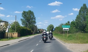 Drogą jadą dwa służbowe policyjne motocykle, przed nimi drogowskaz z napisem Zduńska Wola.