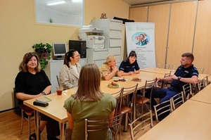 W pomieszczeniu, przy stole siedzą policjanci oraz 4 kobiety. Rozmawiają.