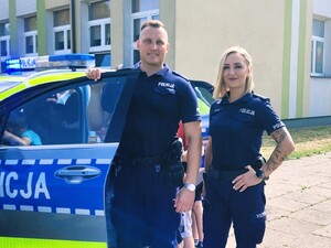 Policjant i policjantka pozują razem do zdjęcia przy radiowozie.