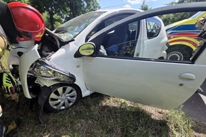Rozbity na drzewie samochód osobowy koloru białego, przy którym widać strażaka.