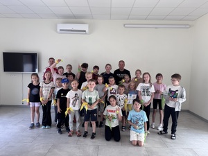 Grupowe zdjęcie dzieci z policjantką podczas letnich półkolonii.