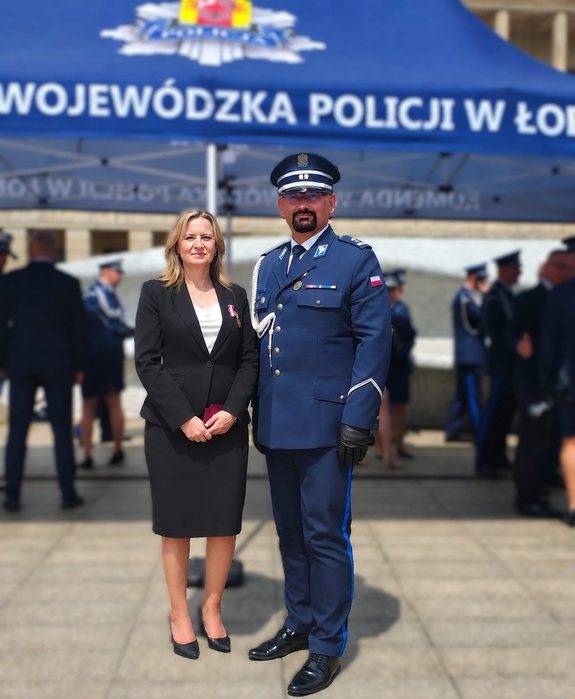 Do zdjęcia pozuje kobieta z medalem i policjant.