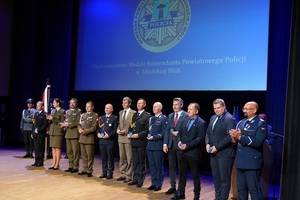 Na scenie stoi grupa osób. Otrzymali okolicznościowy medal. Pozują do zdjęcia.