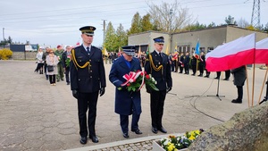 Troje mężczyzn w mundurach idzie pod pomnik. W środku policjant niesie kwiaty.
