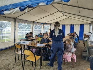 Umundurowana policjantka prowadząca pogadankę na temat bezpieczeństwa wśród dzieci biorących udział w zorganizowanym wypoczynku.