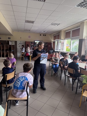 Umundurowana policjantka omawiająca konkurs "Letni PrzeWODNIK", pokazując plakat.