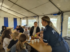 Policjantka  rozdająca dzieciom elementy odblaskowe.
