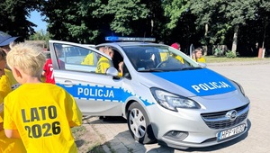 Dzieci stoją obok radiowozu, inne wsiadają do niego.