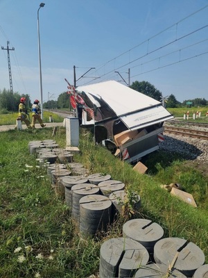 Bus koloru białego leżący z boku torów po zderzeniu z dezyną.