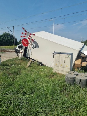 Przewrócony bus na przejeździe kolejowym ze znakiem stop.