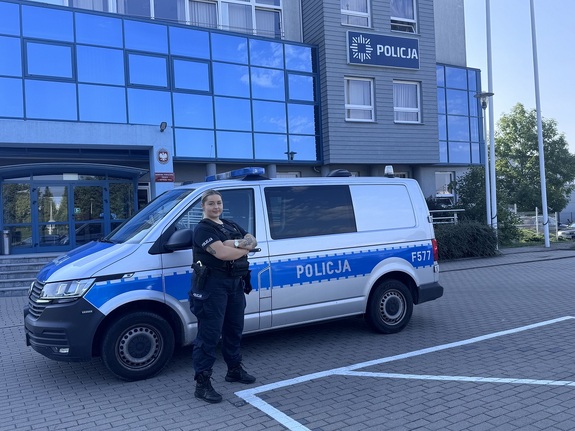 Umundurowana policjantka, stojąca przy oznakowanym radiozie na tle budynku komendy w Zduńskiej Woli.