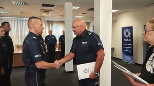 Komendant wręcza policjantowi akt mianowania. W tle widać stojących policjantów.