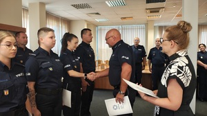 Komendant wręcza policjantce akt mianowania. W tle widać stojących policjantów.