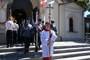 Poczet sztandarowy Policji idzie w pierwszym szeregu po schodach kościoła. Przed pocztem idzie ministrant z krzyżem.