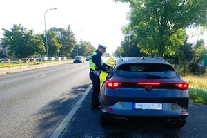 Policjant stoi przy drzwiach kierowcy samochodu.
