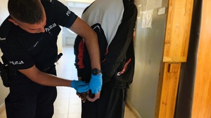 Policjant zakłada kajdanki zatrzymanemu na ręce trzymane z tyłu.