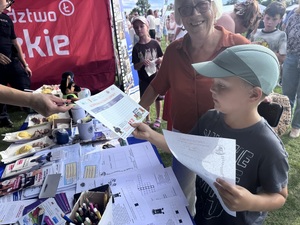 Mały chłopiec przy stoisku policyjnym, odbierający materiały profilaktyczne.