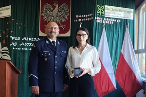 Do zdjęcia pozuje policjant i kobieta, która trzyma medal zamknięty w etui.