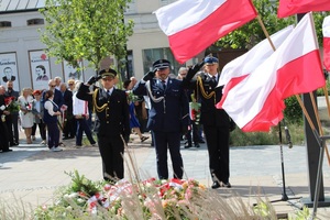 Przed tablicą stoją przedstawiciele służb mundurowych. Salutują.