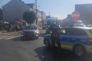 Przejście dla pieszych, na pasach stoi samochód, obok radiowóz i policjant.