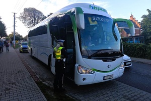 Policjantka rozmawia z kierowcą autobusu. Autobus stoi na zatoczce. W tle radiowóz i chodnik po którym idzie młodzież.