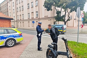 Na chodniku, przy ulicy, policjant kontroluje stan rzeźwości rowerzysty.