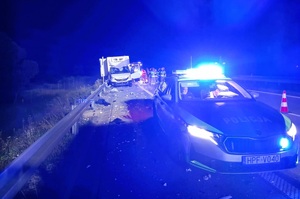 Noc. Droga. Po prawo stoi radiowóz z włączonymi światłami, w tle rozbity samochód ciężarowy, przy nim służby ratownicze