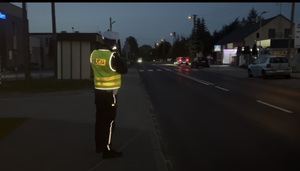 Umundurowany policjant dokonujący pomiaru prędkości w porze wieczorowej.