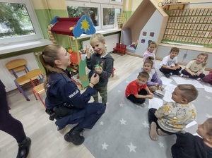 Kursantka pokazująca przedszkolakowi kajdanki i inne wyposażenie policjanta.
