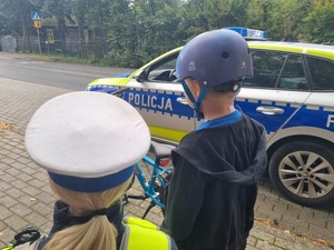 Umundurowana policjantka ruchu drogowego z chłopcem, który otrzymał kask, na tle radiowozu.